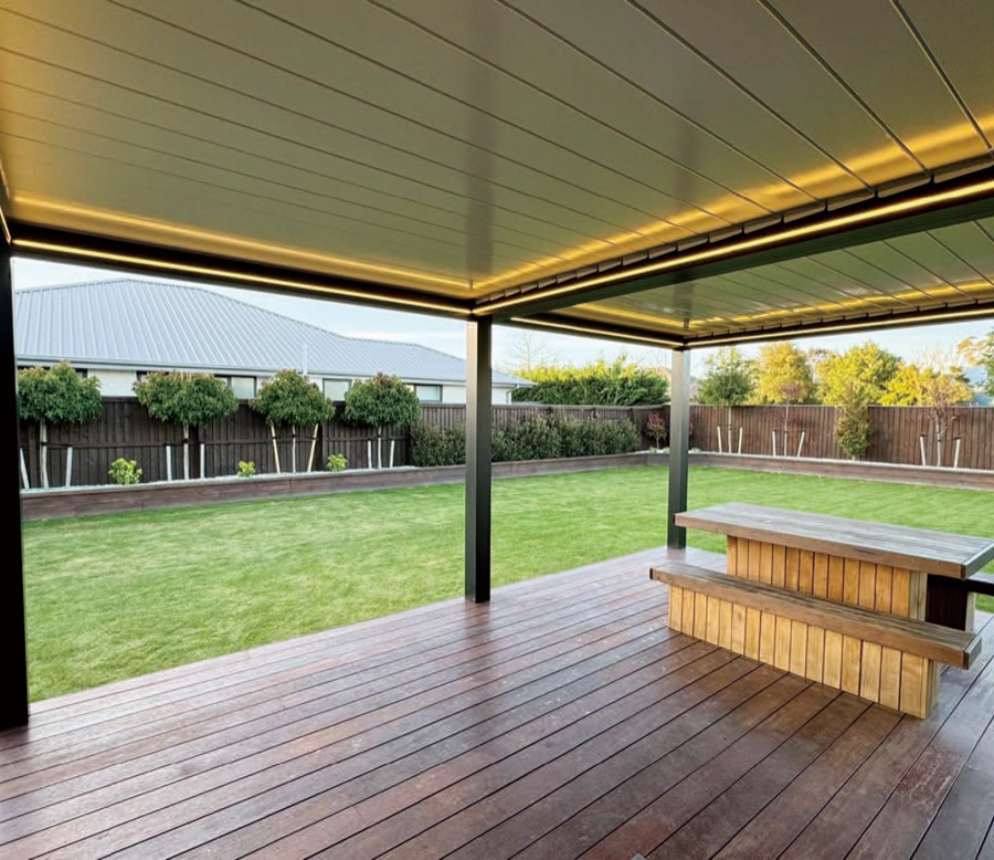 Freestanding aluminium louvre-roof pergola over a timber deck, looking out to a lawn.